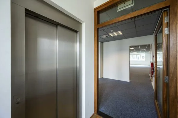 Entree van een modern kantoorpand aan de De Ruijterkade met een gesloten liftdeur en zicht op een lege kantoorruimte.